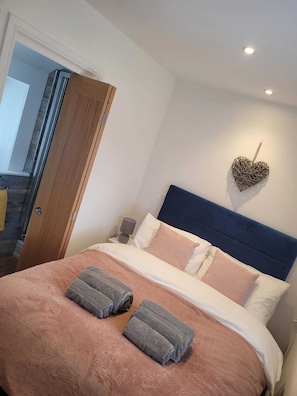 Un dormitorio con una cama, almohadas, una decoración en forma de corazón y una mesita de noche.