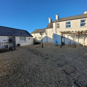 A residential area with a gravel courtyard, a white house with a grey roof, and a blue chair. - Dog Friendly 18th Century Cottage (Saundersfoot)