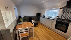 Une cuisine compacte comprenant une table à manger, des chaises, un four encastré et une fenêtre avec des stores.