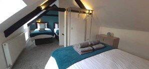 Een slaapkamer met een schuine plafond, een bed met een blauwe dekbedovertrek, een nachtkastje en een hanglamp.
