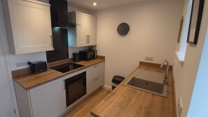 A compact kitchen with white cabinets, a black range hood, a sink, and a clock on the wall. - Dog Friendly 18th Century Cottage (Saundersfoot)