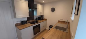A compact kitchen with white cabinets, a black range hood, a sink, and a clock on the wall.