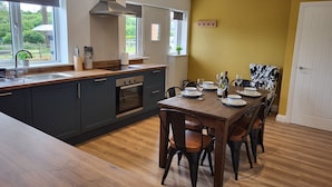 Une cuisine moderne dotée d’un îlot central, d’un four encastré et d’un coin repas avec une table et des chaises en bois.