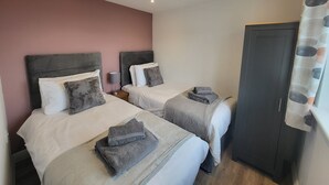 Une chambre d’hôtel avec deux lits, chacun doté d’une tête de lit, d’une table de chevet avec une lampe et d’une serviette grise sur le lit.
