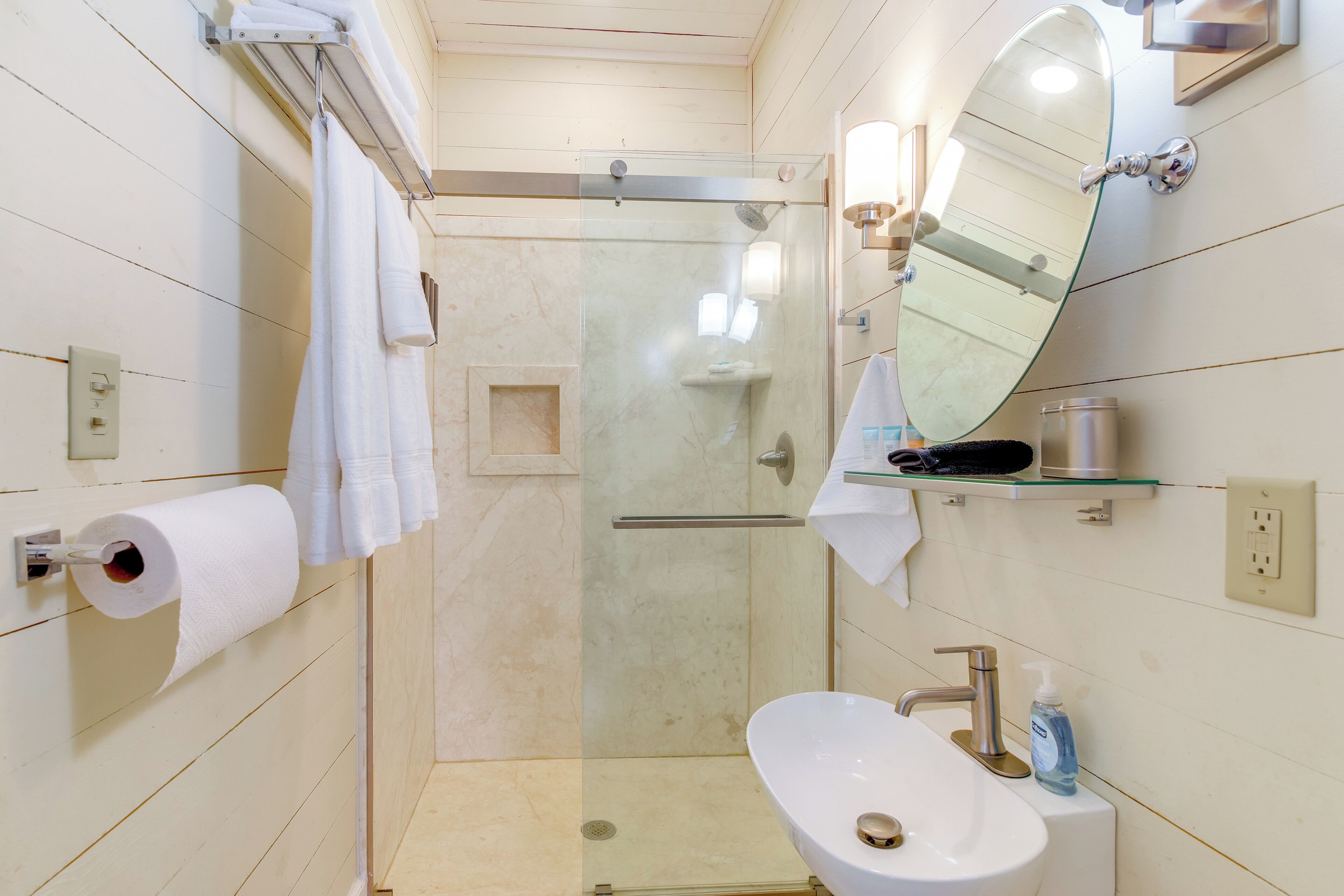 Une salle de bain moderne avec une douche à parois de verre, un lavabo blanc doté d’un robinet argenté et un grand miroir au-dessus du lavabo.