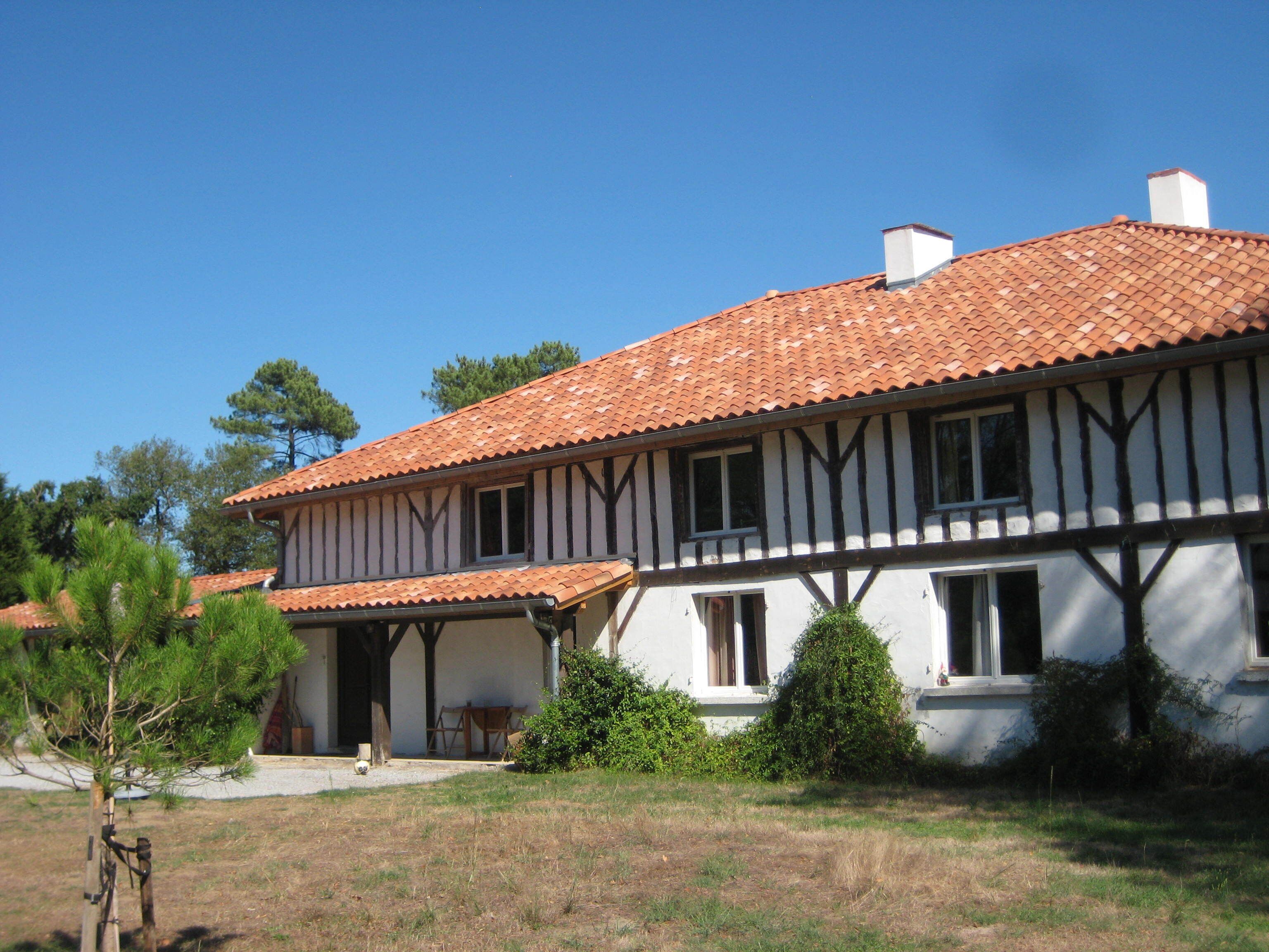 Un bâtiment à deux étages, doté d’un toit recouvert de tuiles, d’un balcon et d’un petit jardin.