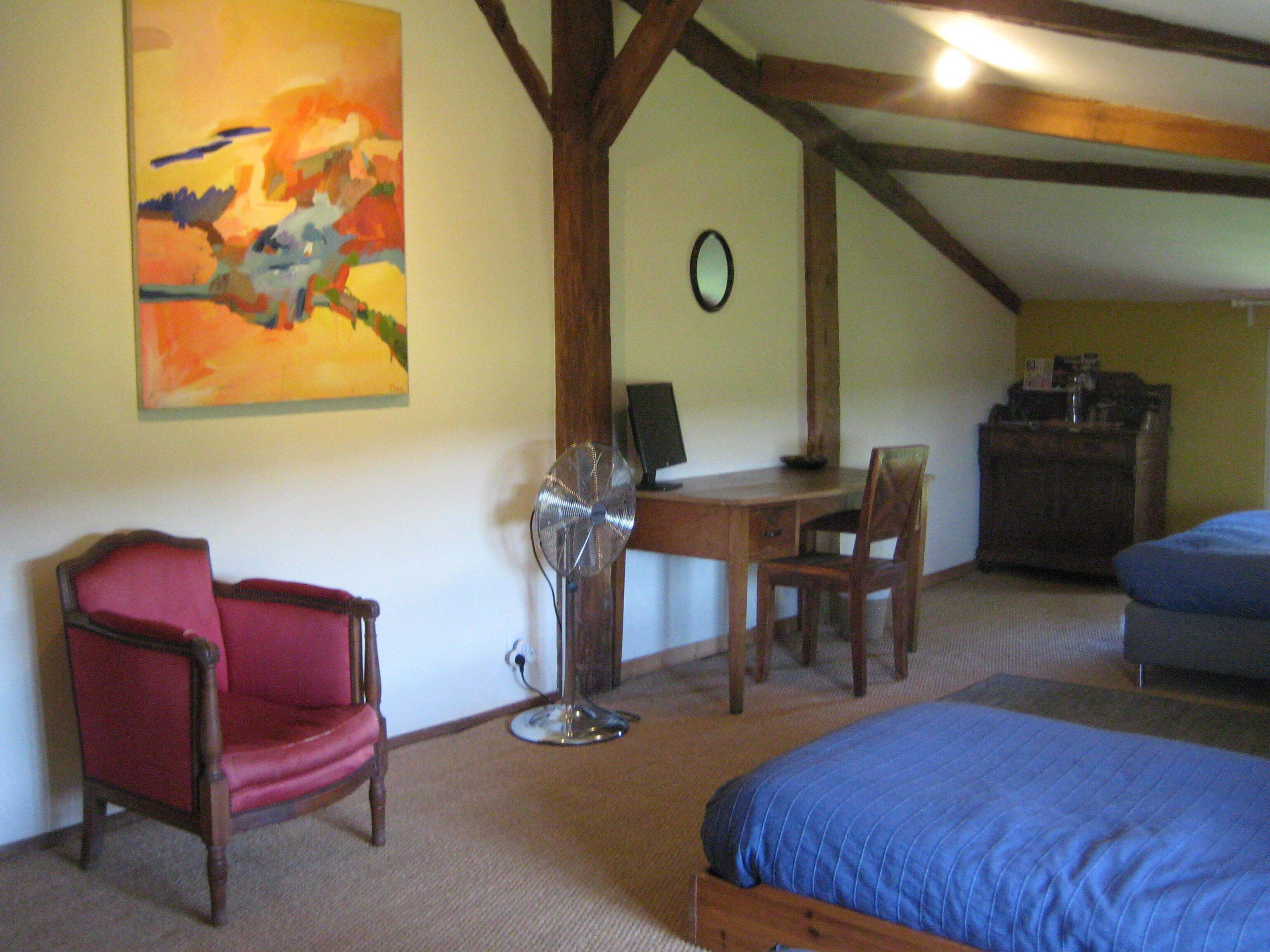 A room with a bed, a desk, a chair, a fan, a clock, and a painting on the wall.