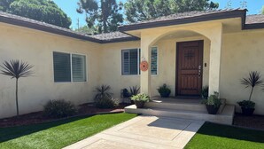 A house with a front yard, a driveway, and a door with a decorative arch. - Charming Craftsman Retreat: 3BR Home w/ Pool & Jacuzzi – Your Perfect Getaway! (Bonita)