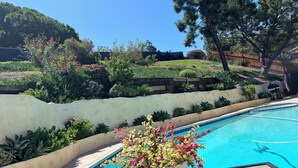 A swimming pool with a white wall and a planter with flowers. - Charming Craftsman Retreat: 3BR Home w/ Pool & Jacuzzi – Your Perfect Getaway! (Bonita)