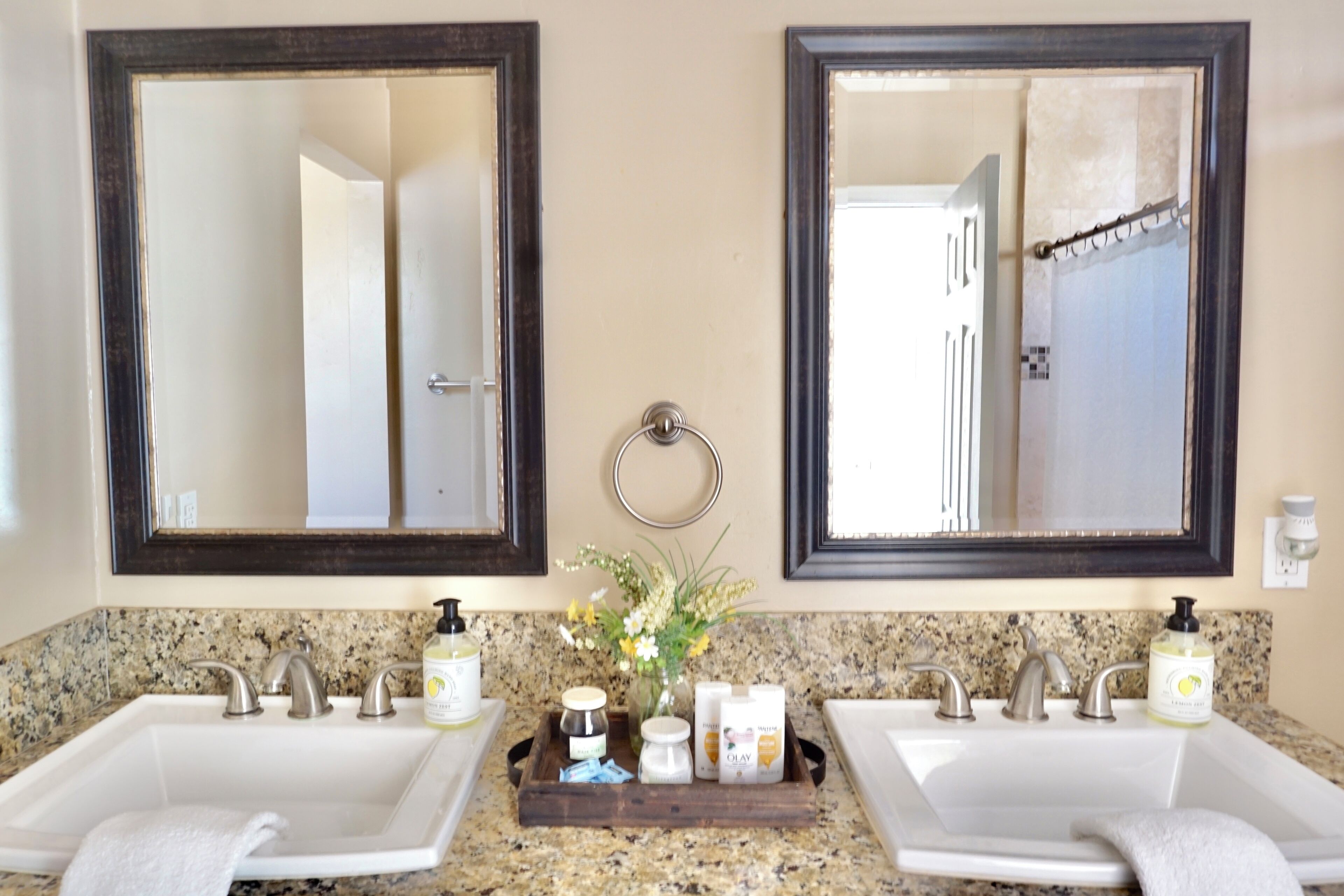 A bathroom with two sinks, each with a mirror above. There is a wooden tray with toiletries and a vase of flowers between the sinks.