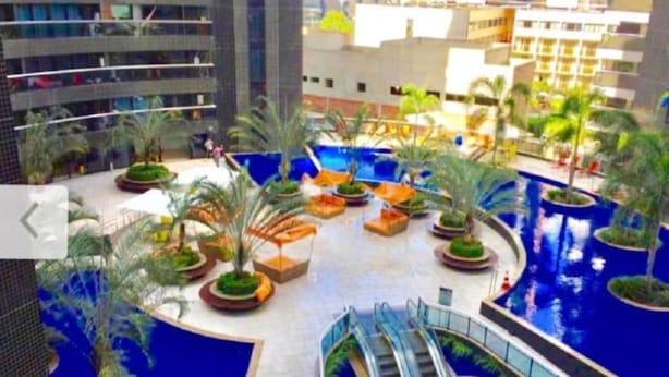 A modern hotel atrium with a central pool, surrounded by palm trees and seating areas. - Beira Mar Fortaleza Landscape Luxo (Meireles Fortaleza)