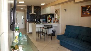 A modern living room with a blue sofa, a kitchen area with a marble backsplash, and a dining space with two bar stools. - Beira Mar Fortaleza Landscape Luxo (Meireles Fortaleza)