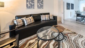 A modern living room with a black leather sofa, a glass coffee table, and a patterned rug. - Connaught Road House in Aldershot (Aldershot)