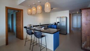 Une cuisine moderne dotée d’un îlot central, de tabourets de bar, de luminaires suspendus et d’un réfrigérateur.