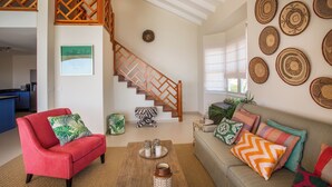 Un vaste espace de vie agrémenté d’un escalier en bois, d’un fauteuil rouge, d’un canapé beige et d’un mur décoré de paniers tressés.