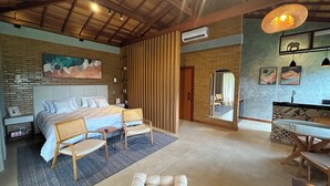A bedroom with a large bed, two chairs, a small table, a mirror, and a bathroom with a sink and decorative tiles. - Green Village - Luxury and Comfort you are looking for! (Corrêas Petrópolis)