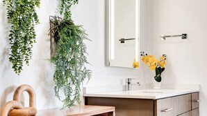 A bathroom with a wooden vanity, a mirror, and hanging plants.