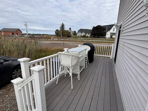 A covered outdoor deck with a table and chairs, a grill, and a view of the surrounding area including houses and a road. - Steps to Beach seaside retreat. 3BR 2BA home where comfort meets charm; (Hampton)