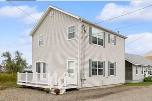 A two-story house with a front porch, a small garden, and a gravel driveway. - Steps to Beach seaside retreat. 3BR 2BA home where comfort meets charm; (Hampton)