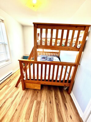 A bunk bed with a wooden frame and a mattress with a nautical-themed pillow. - Steps to Beach seaside retreat. 3BR 2BA home where comfort meets charm; (Hampton)