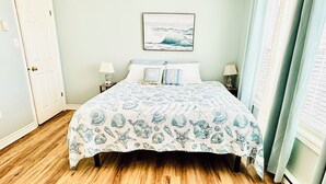 Ein Schlafzimmer mit einem Bett, zwei Nachttischen, einem Schreibtisch und einem gerahmten Bild an der Wand sowie einer Tür.