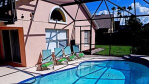 A swimming pool with lounge chairs, a covered patio, and a view of palm trees.