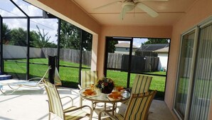 A covered patio with a table and chairs, a ceiling fan, and a view of a backyard.