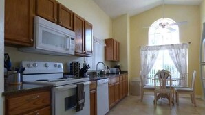 A kitchen with wooden cabinets, a microwave, stove, and a dining area with a chair and table.