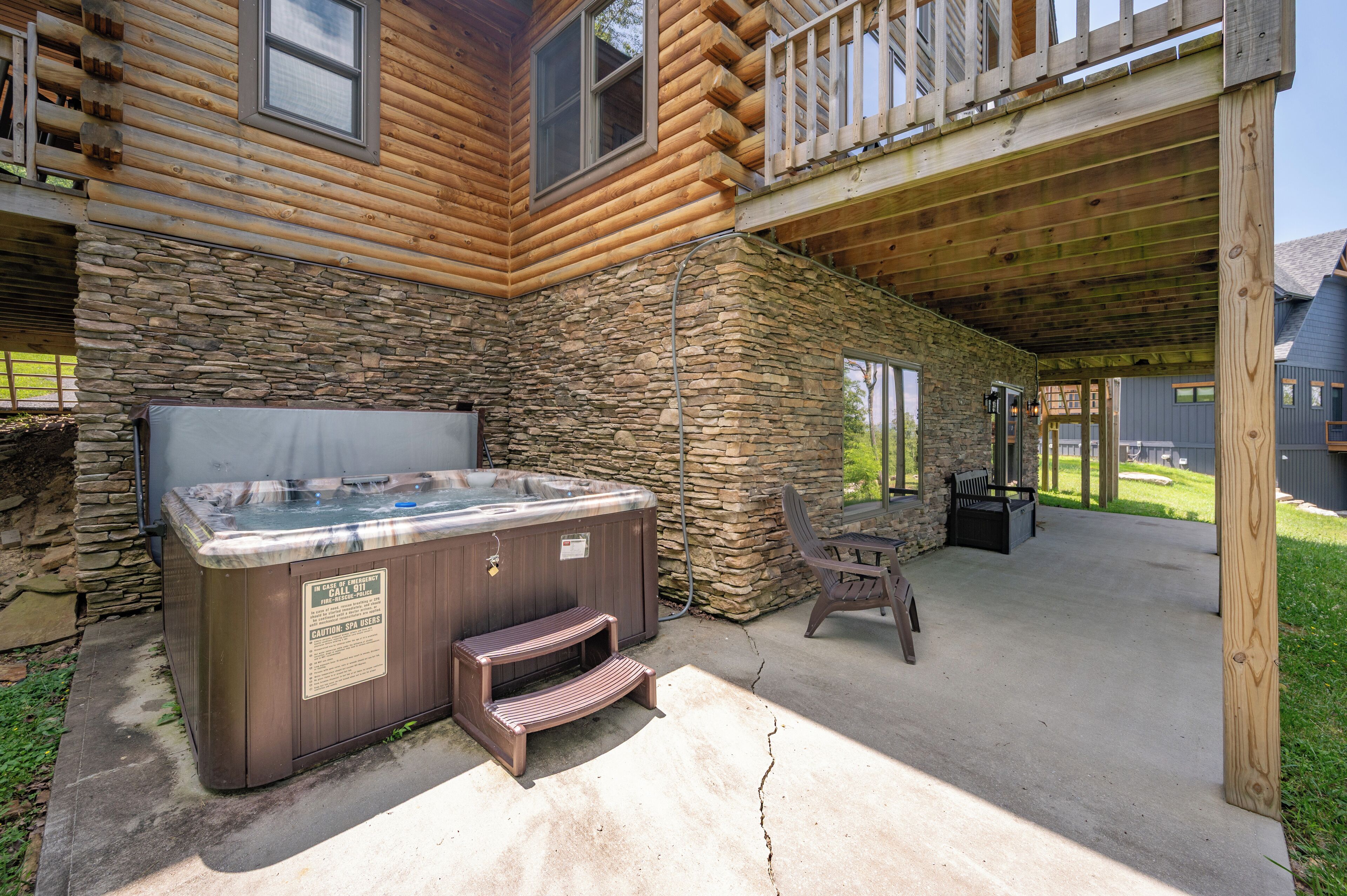 A wooden cabin with a stone exterior, a hot tub, and a covered patio area.