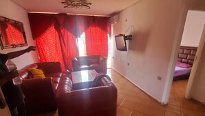 A living room with a red sofa, a glass coffee table, and a ceiling fan. - 🌴 Typical Riad | Historic Center 🏡 Private Terrace | Wi-Fi + Air Conditioning (Marrakech)