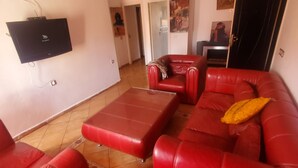 A living room with a red sofa set, a glass coffee table, and a flat-screen TV mounted on the wall. - 🌴 Typical Riad | Historic Center 🏡 Private Terrace | Wi-Fi + Air Conditioning (Marrakech)