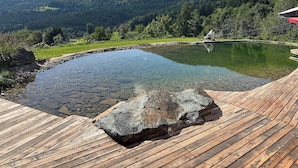 Una terraza de madera con una piscina cristalina rodeada por un paisaje natural.