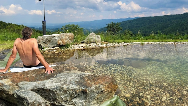 Una persona sentada junto a una piscina cristalina, con vistas a una montaña al fondo.