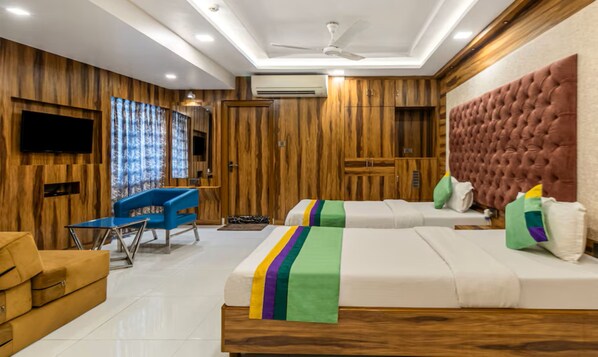 Habitación de hotel con paneles de madera, ventilador de techo, televisor de pantalla plana, sofá, cama con ropa de cama colorida y una mesita.