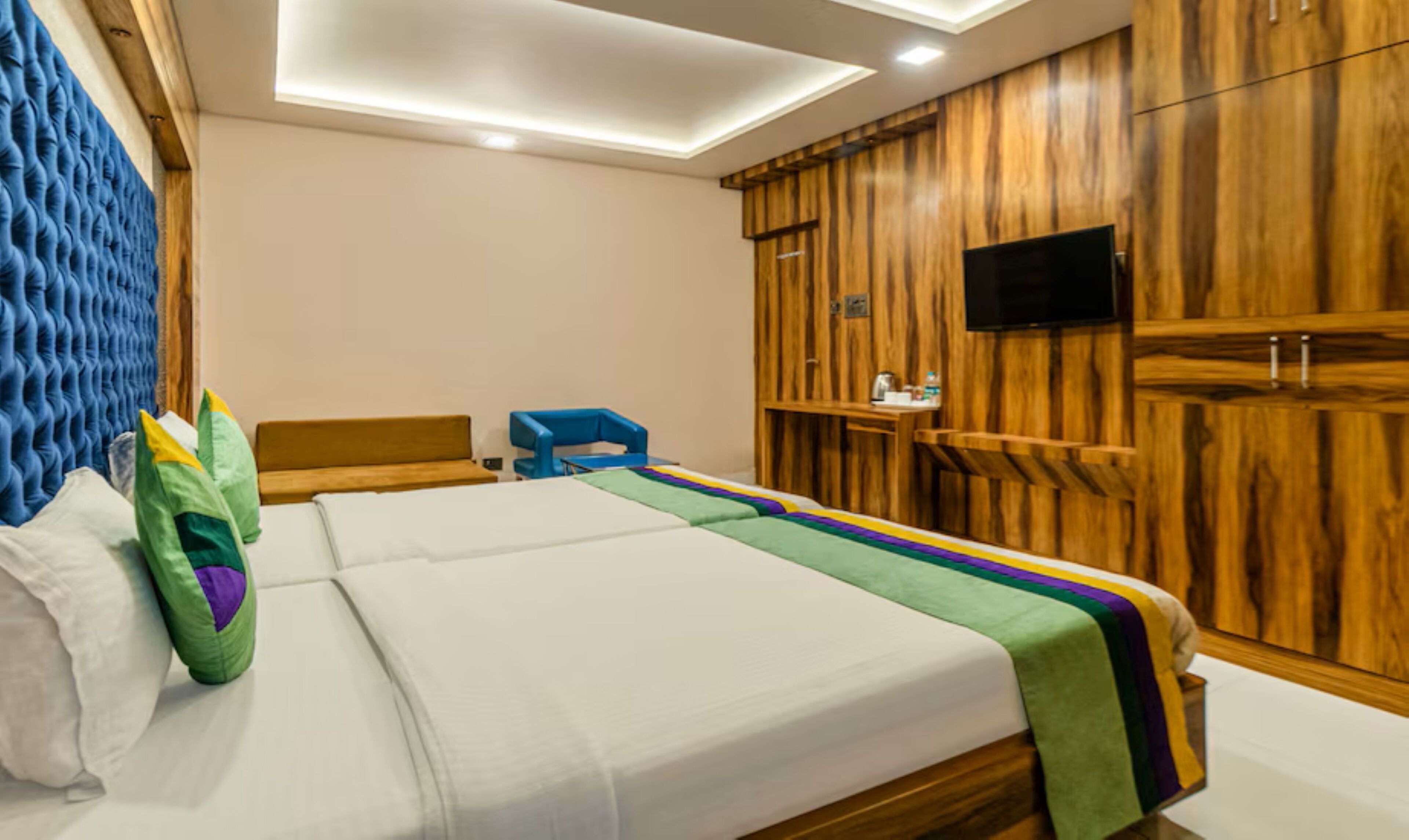 A hotel room with a bed, a TV, wooden paneling, and a ceiling light.