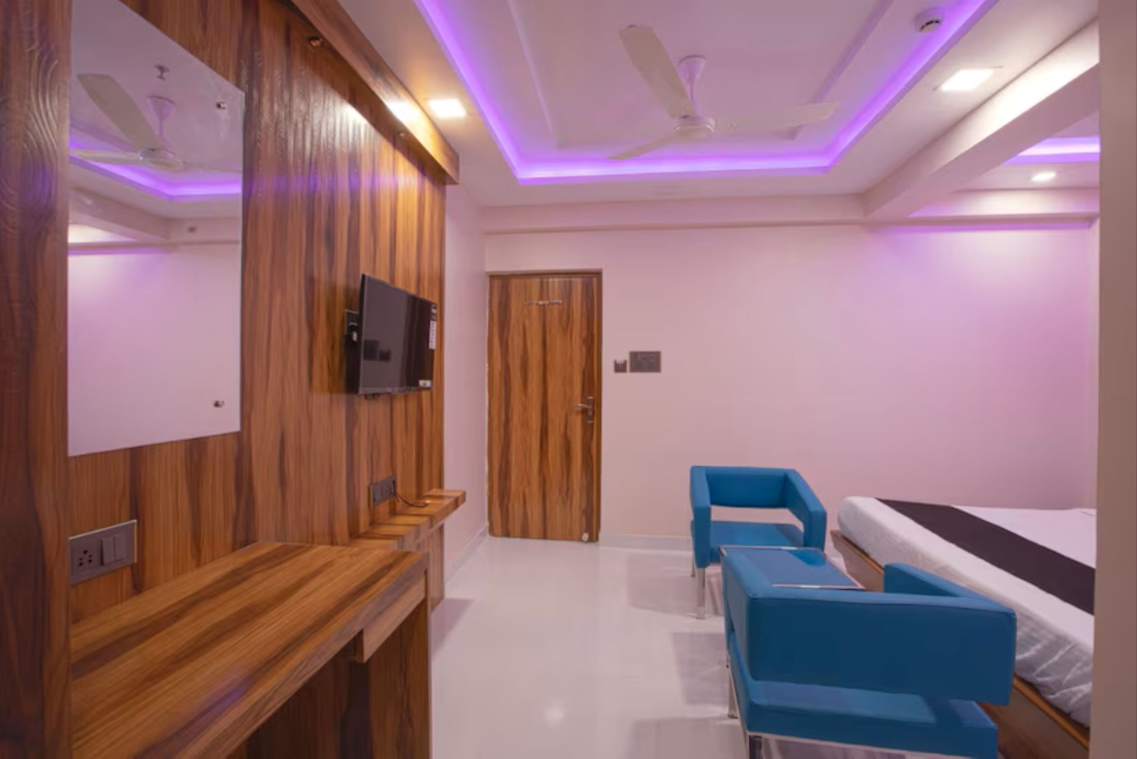 A modern room with a wooden reception desk, a television, a door, and a bed with a blue chair.