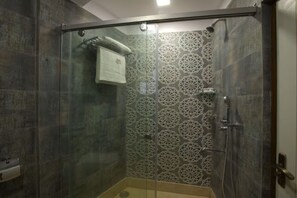Une douche fermée par des parois en verre, dont les murs sont recouverts de carreaux disposés selon un motif géométrique.