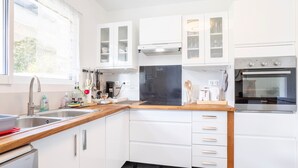 A modern kitchen with white cabinets, a stainless steel sink, a built-in oven, and a window with sheer curtains. - Holiday Home 'Maison Avec Terrasse Et Jardin' with Private Terrace, Private Garden and Wi-Fi (Saint-Yvi)