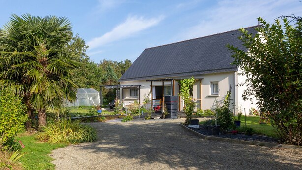 A house with a gravel driveway, a garden with various plants, and a greenhouse in the background. - Holiday Home 'Maison Avec Terrasse Et Jardin' with Private Terrace, Private Garden and Wi-Fi (Saint-Yvi)