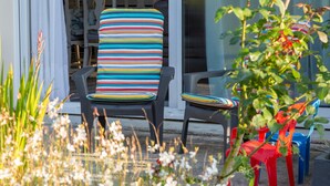 A patio area with outdoor seating, including a chair with a striped cushion and a red chair. - Holiday Home 'Maison Avec Terrasse Et Jardin' with Private Terrace, Private Garden and Wi-Fi (Saint-Yvi)