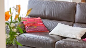 A brown leather sofa with two pillows, one red and one white, in a room with a window. - Holiday Home 'Maison Avec Terrasse Et Jardin' with Private Terrace, Private Garden and Wi-Fi (Saint-Yvi)