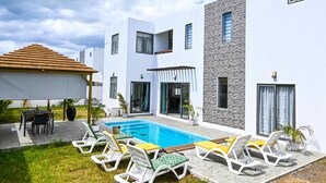 Et moderne hus med swimmingpool, udendørs møbler og en patio.