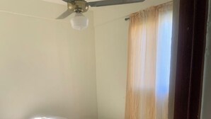 Ein Schlafzimmer mit einem Bett, einem Deckenventilator und einem Fenster mit Vorhängen.