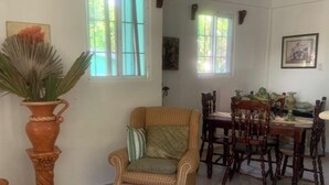 Ein Essbereich mit einem Holztisch und Stühlen, einem Korbsessel und einem Blumentopf.