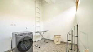 Laundry room with a front-loading washing machine, ironing board, and drying rack.
