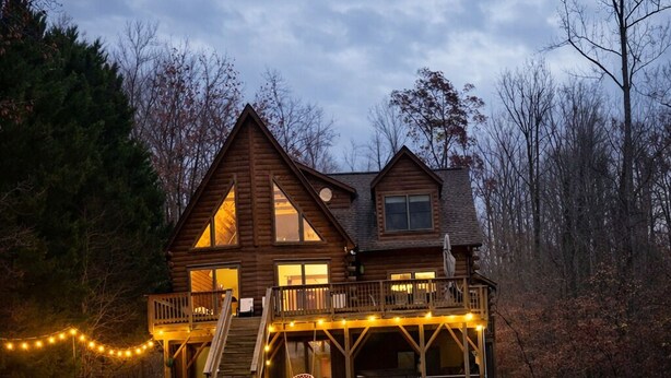 A log cabin with a deck and outdoor seating area with Adirondack chairs around a fire pit.