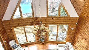 A cozy log cabin interior with a large white sectional sofa, a wooden ceiling, and a view of a wooden deck outside.