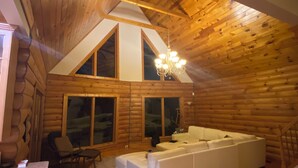 A log cabin interior with a large white sofa, wooden floors, and a chandelier.