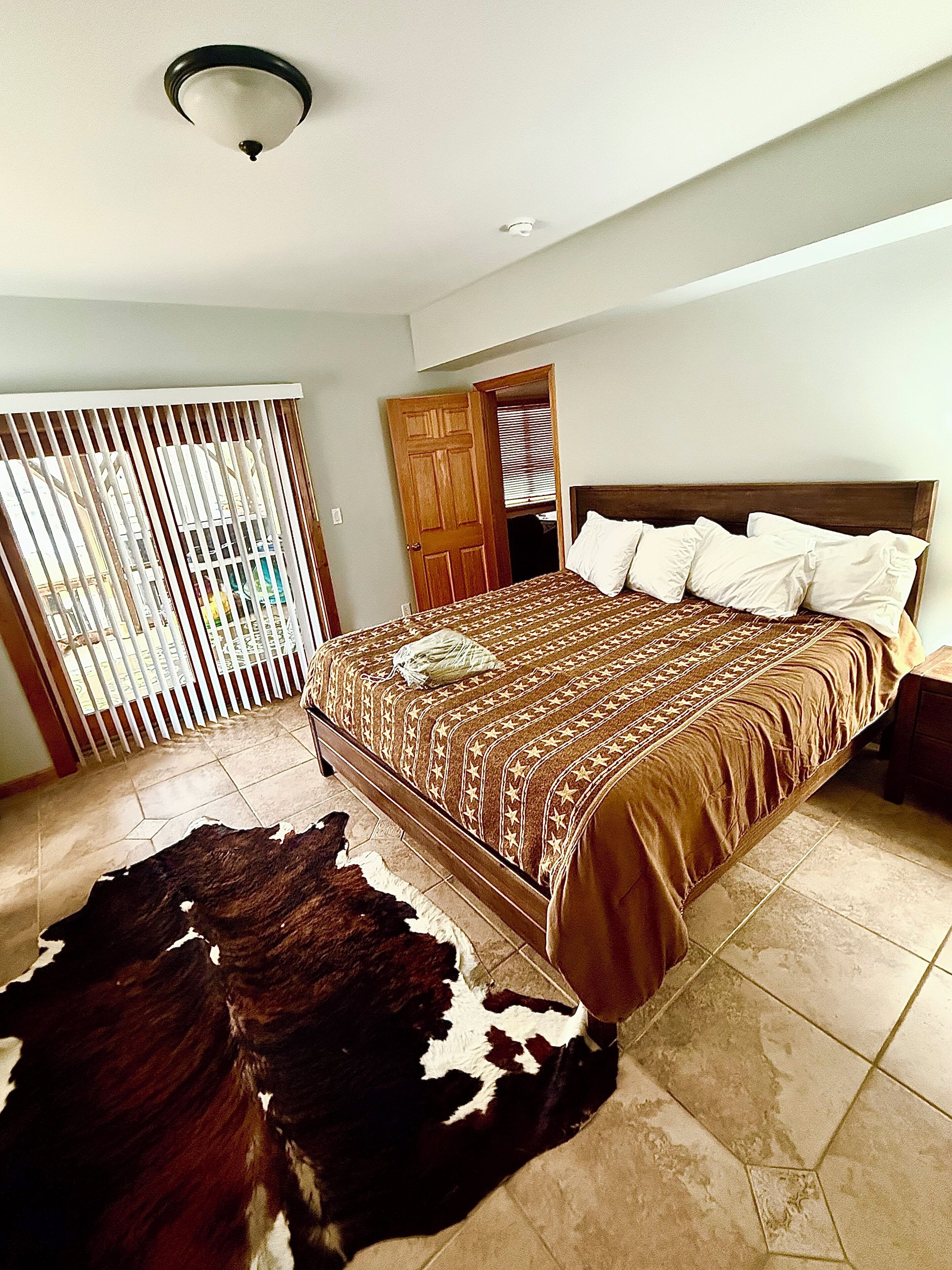 A bedroom with a bed, a wooden headboard, a ceiling light, a door, and a cowhide rug.