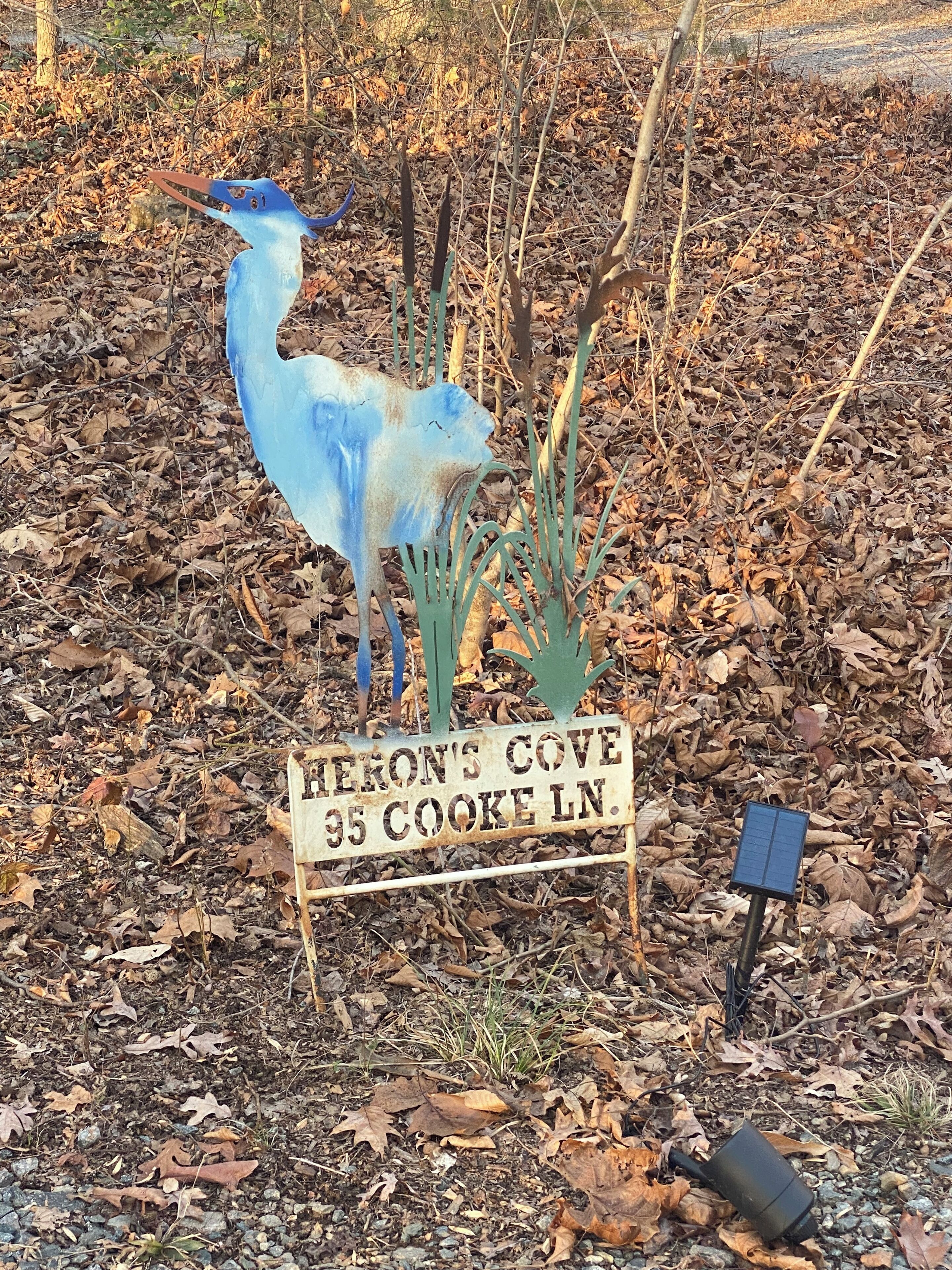 A metal sign with the text "HERON'S COVE 95 COOKE LN."